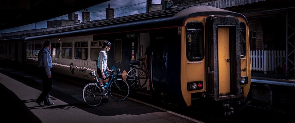 A cyclist wheeling a bike onto a regional train at a UK station platform